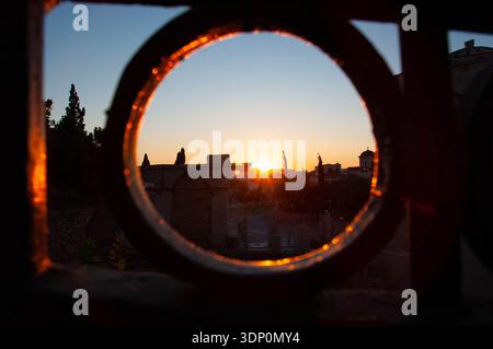 Malerische italienische Sonnenuntergangslandschaft mit Rundzaun, die Silhouetten von Bäumen und Gebäuden vor einem pulsierenden Himmel einfängt. Stockfoto