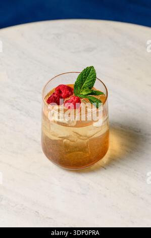 Erfrischender Eistee mit Eiswürfeln, frischen Himbeeren und Minze im Glas. Sommerbeerencocktail mit Eis und Minze auf einer hellen Tischplatte in einem Restaurant Stockfoto
