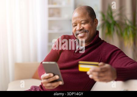 Schwarzer Mann mittleren Alters mit Smartphone und Kreditkarte zu Hause Stockfoto