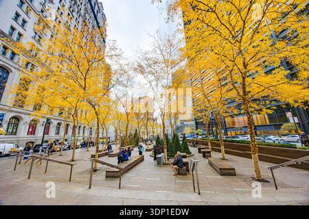 Die Gäste entspannen sich im New York City City Urban plaza mit goldenen Herbstbäumen und festlichen Lichtern, umgeben von Bürogebäuden Stockfoto