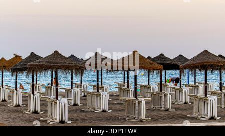 Leerer Strand mit Strohschirmen und zusammengefalteten Liegestühlen entlang der Mittelmeerküste. Costa del Sol, Andalusien, Spanien – 1. Mai 2025 Stockfoto