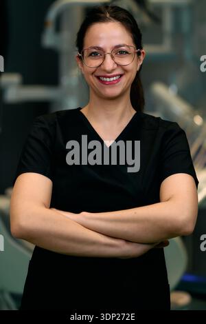 Selbstbewusste Frau im Gesundheitswesen in Scrubs lächelt mit überkreuzten Armen in der Klinik Stockfoto