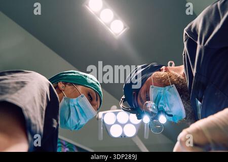 Chirurgen im OP tragen Masken und Scheinwerfer unter hellen Deckenlichtern für Eine medizinische Operation Stockfoto