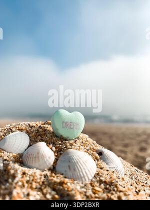 Flacher Blick auf ein Süßwarenherz mit dem Wort 'Traum' drauf in Sand an einem Strand an einem sonnigen Tag Stockfoto