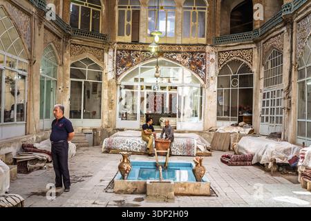 KASHAN, IRAN - 13. AUGUST 2016: Teppichverkäufer sitzen in einer überdachten Gasse des Kaschan Basars im Iran, umgeben von persischen Teppichen und traditionellem Dekor, auf TRA Stockfoto