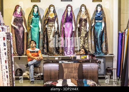 ISFAHAN, IRAN - 20. AUGUST 2016: Zwei Ladenbesitzer sitzen in einem Stoffgeschäft auf dem Isfahan Basar unter Schaufensterpuppen in bodenlangen Kleidern auf dem iranischen wo Stockfoto