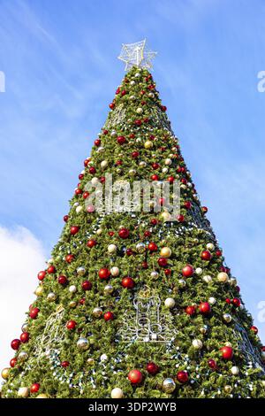 Großer Weihnachtsbaum mit roten und gelben Kugeln aus Kunststoff Vor dem Hintergrund des blauen Himmels Stockfoto
