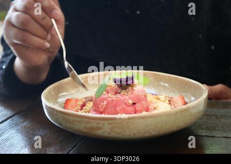Eine Person schmeckt ein Dessert mit Eis, Obst und einer Garnitur in einem Café Stockfoto