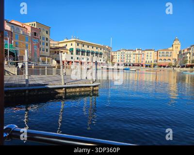 NUR FÜR REDAKTIONELLE ZWECKE - ORLANDO FLORIDA: ​View von einem Wassertaxi, das sich dem hölzernen Dock im Loews Portofino Bay Hotel in Orlando, Florida nähert. Das Foto zeigt die lebhaften gelben und Terrakotta-Gebäude des italienischen Resorts und verschiedene kleine Boote, die im Hafen verankert sind. Stockfoto