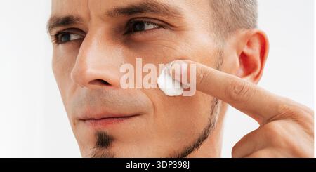 Eine Nahaufnahme eines attraktiven Mannes mit gesunder Haut, die Anti-Falten oder Anti-Aging-Creme aufträgt. Stockfoto