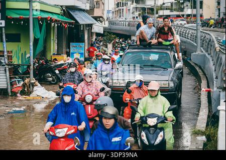 Eine Straßenszene, in der Menschen bei starkem Regen in Asien Motorräder auf einer überfluteten Straße fahren. Nha Trang, Vietnam - 21. November 2025. Stockfoto