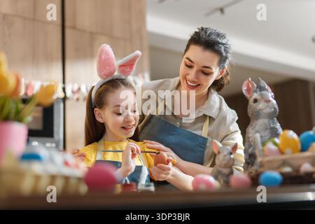 Mutter und Tochter genießen schöne Zeit beim Malen von Ostereiern. Lächeln und Freude erfüllen die Luft, während sie den festlichen Geist in ihrer gemütlichen Küche genießen Stockfoto