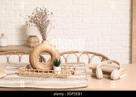 Tablett mit einer Vase mit trockenen Blumen, Büchern und Kopfhörern auf dem Tisch im modernen Speisesaal Stockfoto