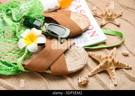 Schnur-Tasche mit Flasche Sonnencreme, Magazin und Strandaccessoires auf Sand als Hintergrund, Nahaufnahme Stockfoto