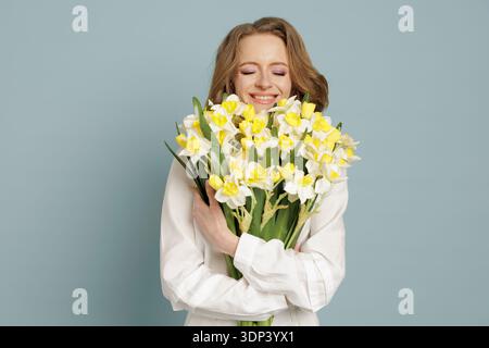 Lächelnde Frau mit einem Strauß Narzissen im Studio. Ideal für Frühjahrsaktionen, Lifestyle-Branding und saisonale Werbekampagnen. Stockfoto