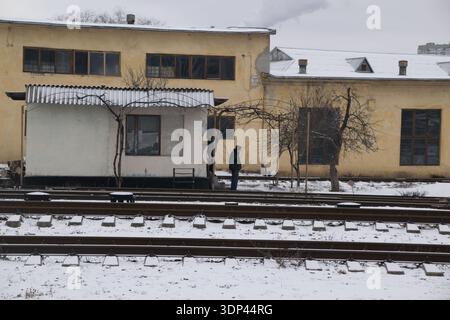 Der Bahnhof in Chisanau Moldau zeigt Schnee auf dem Boden. Ein Mann steht in der Nähe eines kleinen Gebäudes in einer ruhigen Szene im Winter. Stockfoto