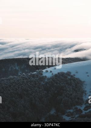 Blick auf eine schneebedeckte, bergige Landschaft, wo die Wolken auf die Erde treffen und einen ruhigen und doch starken Kontrast zwischen weiß und Dunkelheit schaffen, Stosswihr Stockfoto