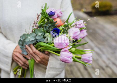 Nahaufnahme einer Frau mit einem großen Strauß aus violetten Tulpen und orangefarbenen Ranunkeln mit Kopierraum. Weiches Blumenmuster im Frühling Stockfoto