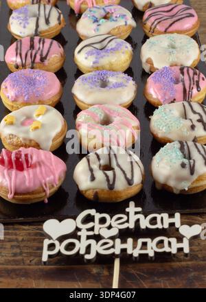 Mini-Donuts mit Schokolade und Dekoration. Daneben befindet sich der Text in serbischer Sprache "Срећан рођендан" (alles Gute zum Geburtstag auf Serbisch). Stockfoto