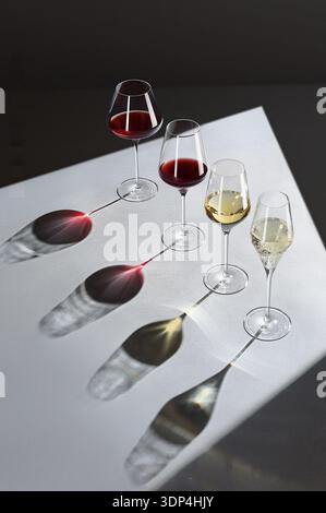 Hochwinkelansicht von verschiedenen Weingläsern, die lange künstlerische Schatten auf grauer Oberfläche werfen Stockfoto