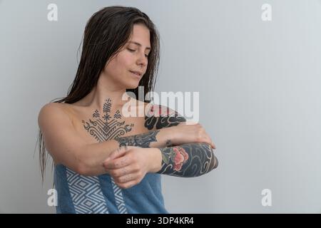 Frau, die nach dem Duschen Tätowierungen auf Armen und Brust bewundert Stockfoto