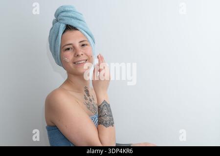 Junge Frau, die Gesichtscreme mit feuchtigkeitsspendender Hautpflege aufträgt Stockfoto
