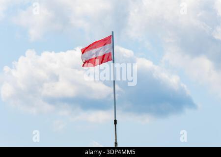 Rot-weiße österreichische Flagge winkt im Wind gegen blauen Himmel mit Wolken Stockfoto