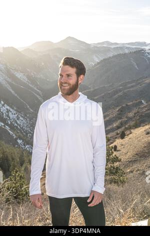 Ein bärtiger Mann genießt einen sonnendurchfluteten Berggipfel. Stockfoto