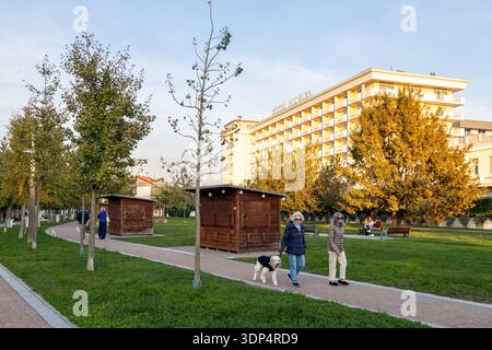 Abano Terme, Italien - 28. Oktober 2025: Menschen, die auf den Pfaden des Parco Urbano Termale spazieren gehen, mit Hotel All'Alba im Hintergrund Stockfoto