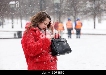 Junge Frau im roten Mantel mit Smartphone auf der Winterstraße Stockfoto