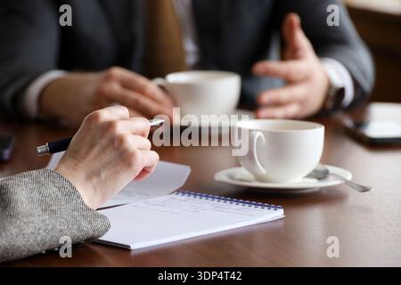Leute, die am Tisch mit Teetassen reden, Frau mit Stift und Mann im Business-Anzug. Konzept des Geschäftstreffens, der Diskussion, des Gesprächs Stockfoto