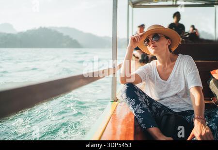 Junge Reisende mit Strohhut und Sonnenbrille, die auf einem Langboot sitzt und die malerische Aussicht auf den Khao Sok Nationalpark Cheow Lan Lake in Thailand du genießt Stockfoto