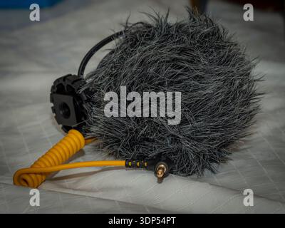 Nahaufnahme eines professionellen Mikrofons mit Windschutzscheibe und gelbem Spiralkabel für Audioaufnahmen im Freien. Stockfoto