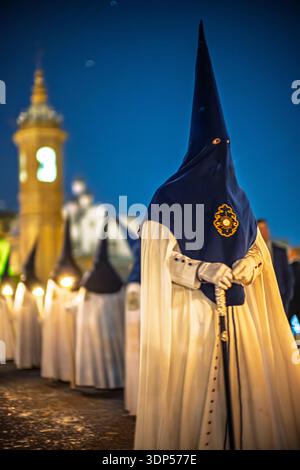Ein Nazarener aus der La Estrella Bruderschaft, ein Abgeordneter der Sektion, beobachtet die Karwoche Prozession in der Palmennacht in der Nähe der Carmen Kapelle der Triana-Brücke. Stockfoto