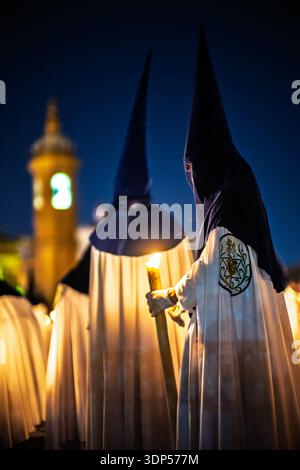 Nazarener aus der Bruderschaft La Estrella beleuchten die Carmen-Kapelle neben der Triana-Brücke während der Palmensonntagsprozession in der Nacht in Sevilla, S. Stockfoto