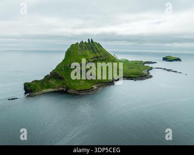 Aus der Vogelperspektive sehen Sie smaragdgrüne Hänge, die zum Meer herabstürzt, die zerklüftete Insel Tindhólmur, die stolz auf das weite Meer, die Färöer Inseln, steht. Stockfoto