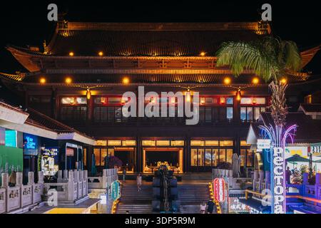 Großes traditionelles chinesisches Holzgebäude mit warmer Beleuchtung in der Nacht in Sanya Stockfoto