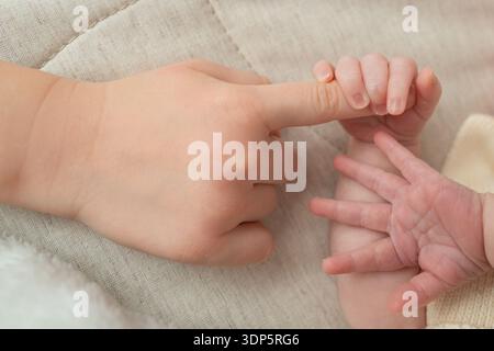 Nahaufnahme einer Neugeborenen-Hand, die den Finger eines älteren Kindes sanft hält. Das Bild konzentriert sich auf Verbindung, Fürsorge und Familienbindung und symbolisiert Stockfoto