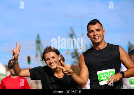 Freudige Läufer posieren mit Friedenszeichen während eines sonnigen Stadtrennens Stockfoto