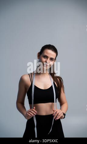 Eine junge Frau posiert in schwarzer Sportswear mit einem Maßband um den Hals Stockfoto