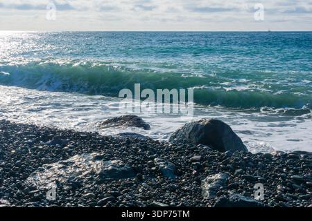 Wellen brechen am Kieselstrand mit Felsen Stockfoto