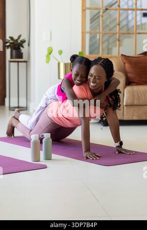 Afroamerikanische Mutter und Jugendtochter halten eine Planke auf lila Matte zu Hause helle Aktivkleidung Stockfoto