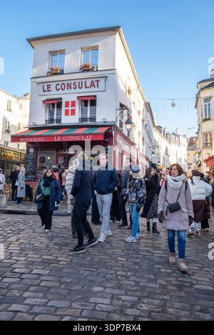 Paris, Frankreich; Dezember 30 2025: Touristen gehen am historischen Café Le Consulat in Montmartre, Paris vorbei. Traditionelle französische Architektur auf A Stockfoto