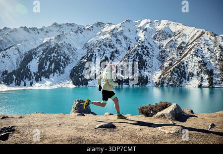 Mann Athlet Runner auf dem Trail im Bergtal am sonnigen Wintertag. Joggen in Sportbekleidung in der Natur Stockfoto