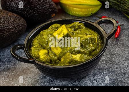 Lebhafte Schüssel mit grünem Palak Paneer, einem indischen Spinat und Käse-Curry. Hochwinkelansicht auf dunkler strukturierter Oberfläche, mit frischer Avocado und Starfru Stockfoto