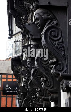 Geschnitzte Köpfe an einer Gebäudefassade an der Foregate Street in Chester, Cheshire. Die Skulpturen im mittelalterlichen Stil befinden sich auf einem Fachwerkgebäude. Stockfoto