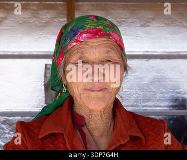 Nahaufnahme eines Porträts einer älteren mongolischen Frau in traditioneller Kleidung, das ihre verwitterten Merkmale und ihr kulturelles Erbe hervorhebt. Stockfoto