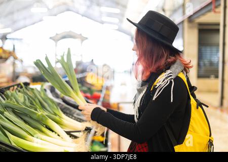 Eine junge Frau, die frischen Lauch auf dem Lebensmittelmarkt wählt Stockfoto