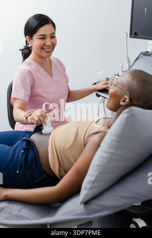 Sonographin mit Sonde an afroamerikanischer Patientin mit Nasenkanüle am Untersuchungstisch Stockfoto