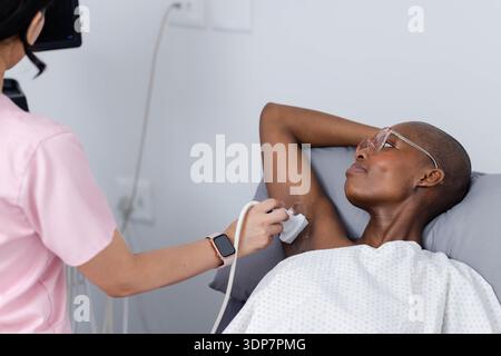 Afroamerikanische Patientin und Technikerin, die Ultraschall mit Sondengel im Untersuchungsraum im Kleid macht Stockfoto